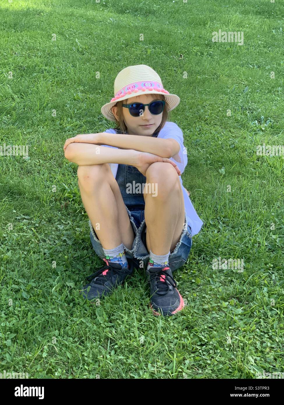 Fille avec chapeau errant assis sur l'herbe. Banque D'Images
