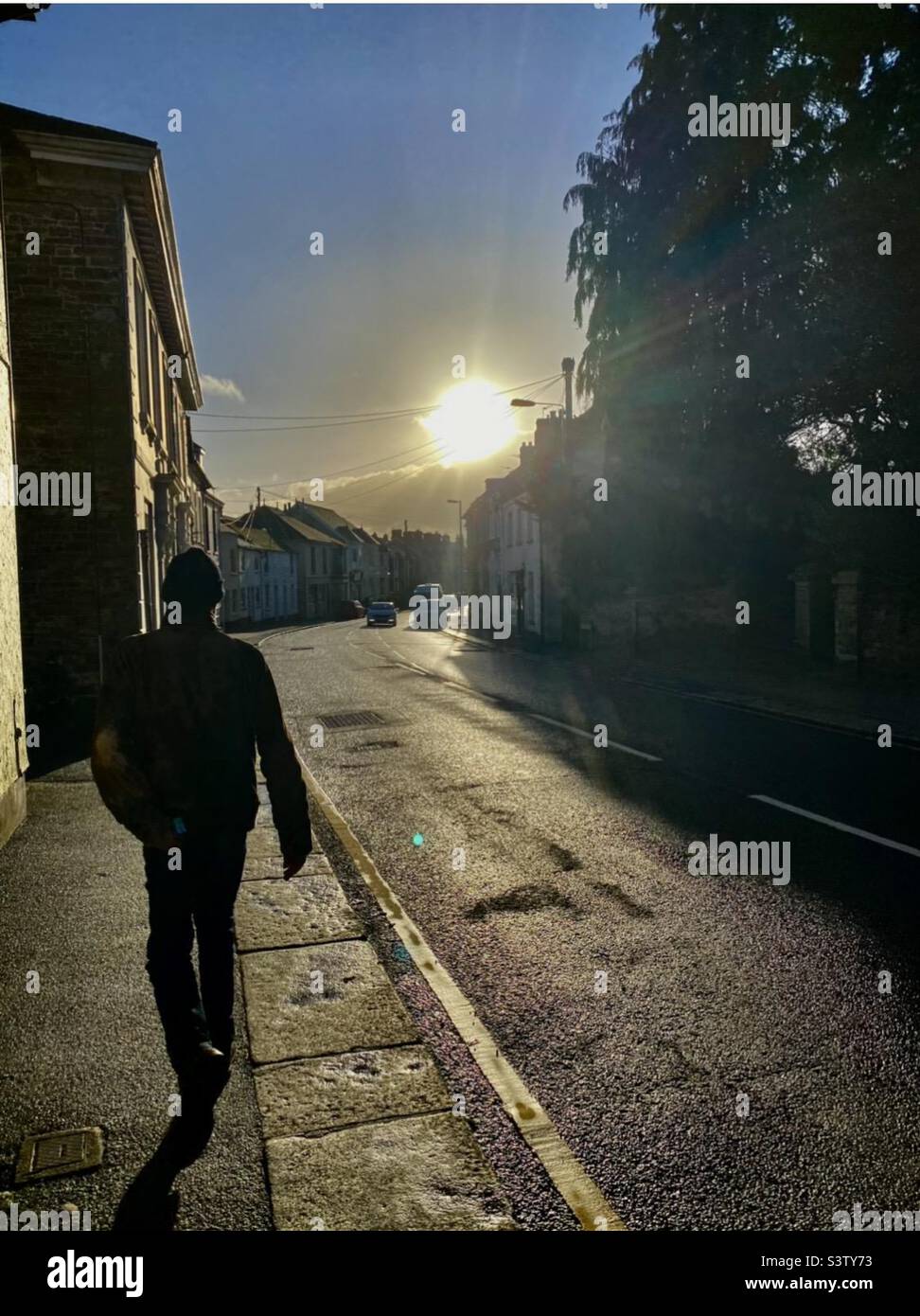 Homme marchant dans une rue de Cornwall sous un froid coucher de soleil d'automne Banque D'Images