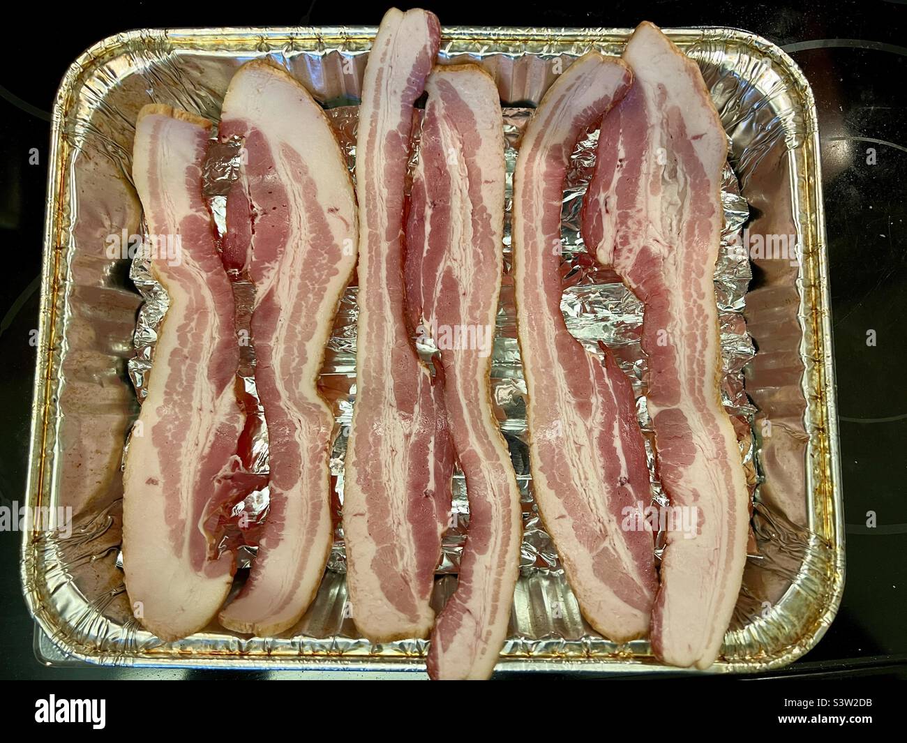 Des tranches de bacon crues dans une plaque en aluminium vont au four pour la cuisson Banque D'Images Des tranches de bacon crues dans une plaque en aluminium vont au four pour la cuisson Banque D'Images