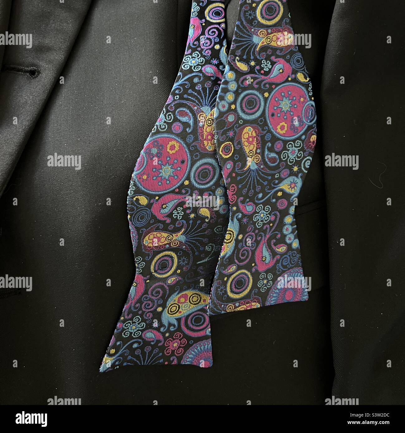 Noeud papillon défait avec motif brodé, reposant sur une veste de smoking noire, prête à être portée pour un événement spécial Banque D'Images