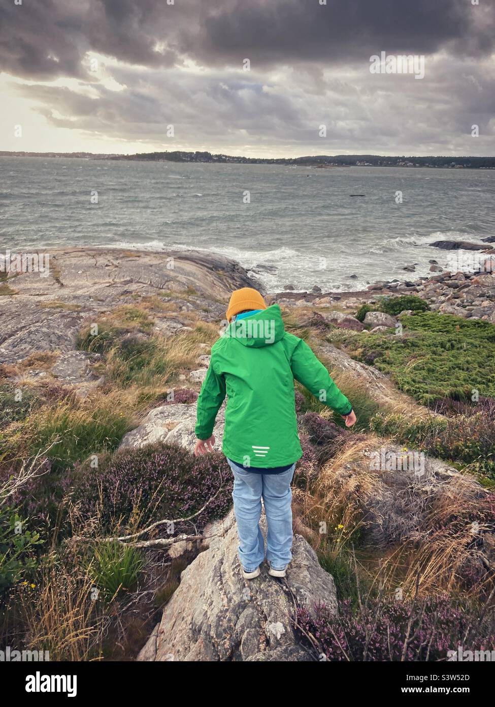 Un garçon de huit à dix ans se brouille dans les rochers de la côte ouest suédoise pendant une tempête - Image de stock capturée avec un smartphone