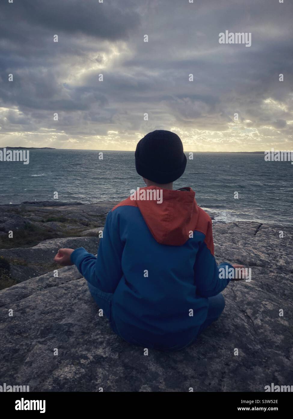 Un garçon âgé de onze ou douze ans qui regarde la mer baltique sur la côte ouest suédoise pendant une tempête dans une pose de yoga Banque D'Images