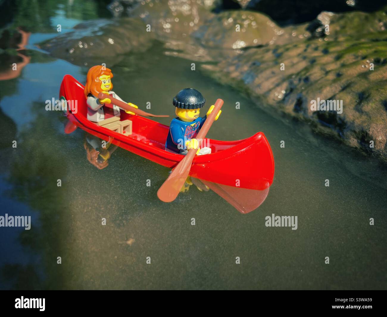 Deux figurines Lego dans un canoë rouge sur l'eau boueuse Banque D'Images