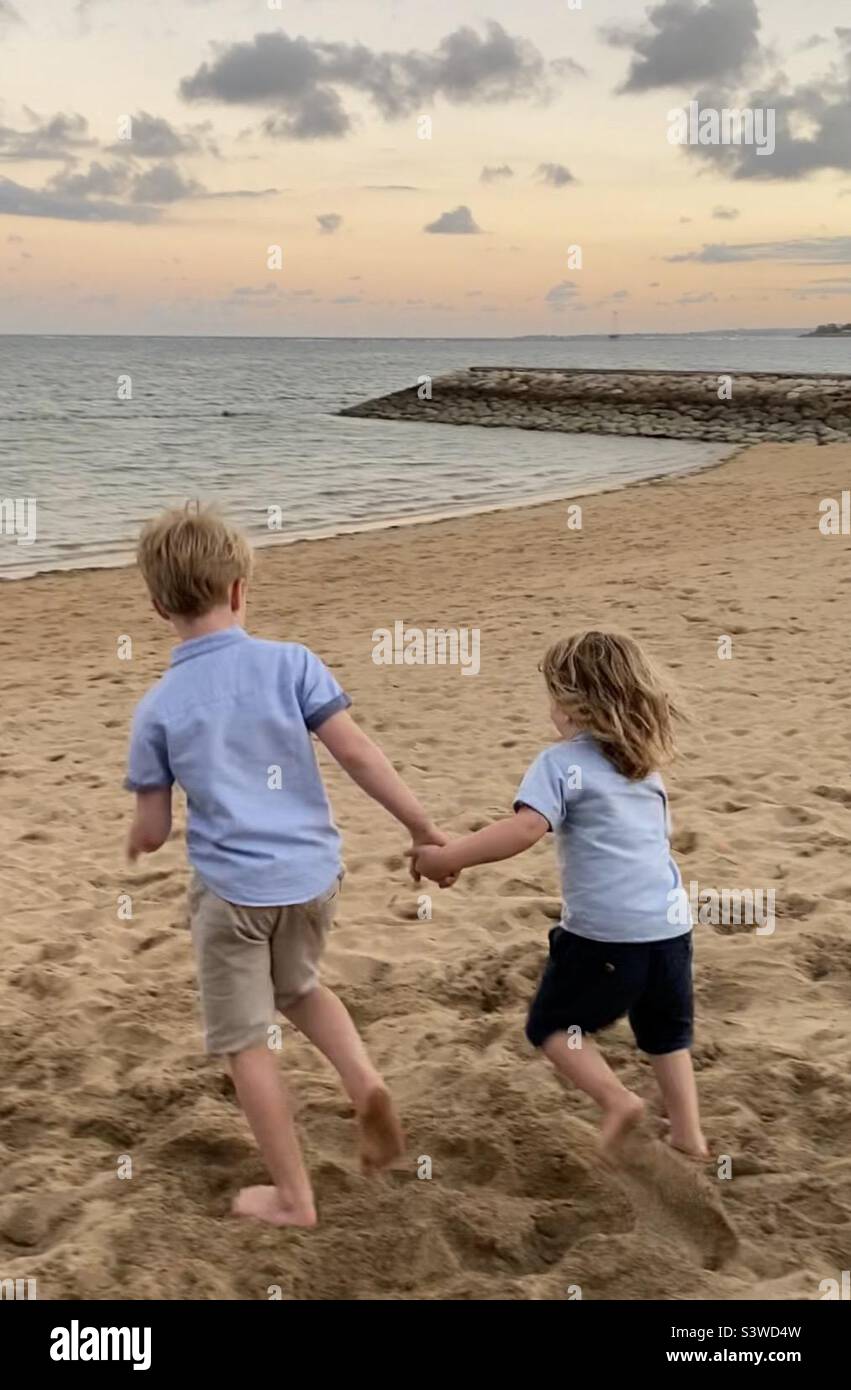 Deux petits garçons tenant les mains courant sur la plage vers la mer Banque D'Images