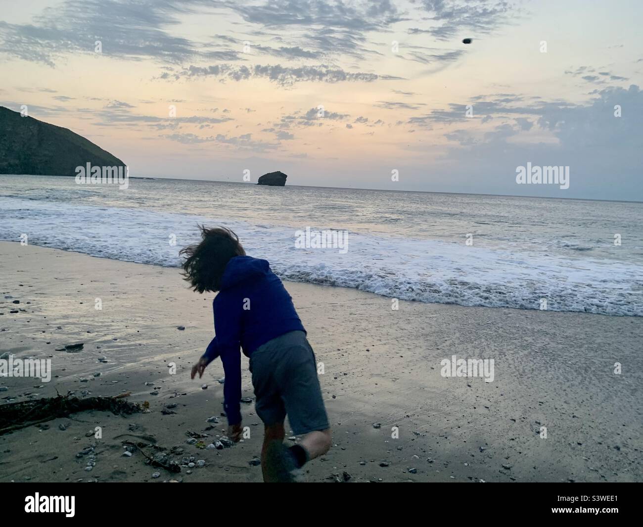Un jeune garçon jette une pierre dans la mer. Banque D'Images