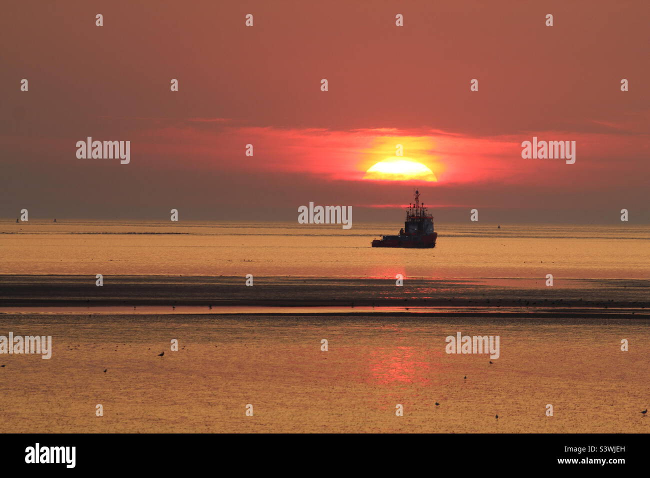 Un beau coucher de soleil sur la plage. Un bateau peut être vu directement sous le soleil rouge tombant. Cette photo a été prise pendant un temps exceptionnellement chaud et une vague de chaleur. - Image de stock capturée avec un smartphone
