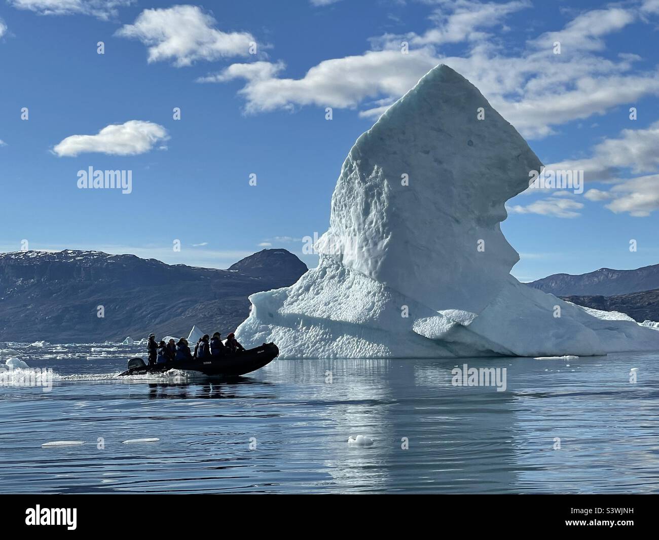 Un bateau de zodiaque approchant un iceberg massif dans un fjord de l'est du Groenland par une journée d'été ensoleillée Banque D'Images