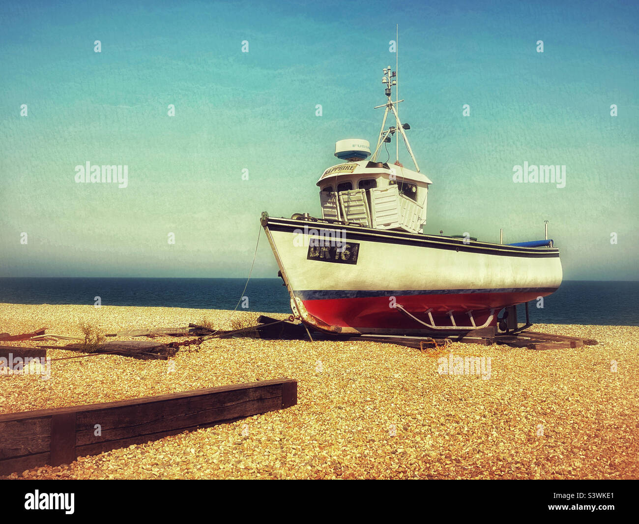 Un ancien chalutier de pêche abandonné se trouve sur une plage de galets sur la côte sud de l'Angleterre. C'est l'été et le soleil brille. Représentation créative d'une scène côtière. Photo ©️ COLIN HOSKINS. Banque D'Images