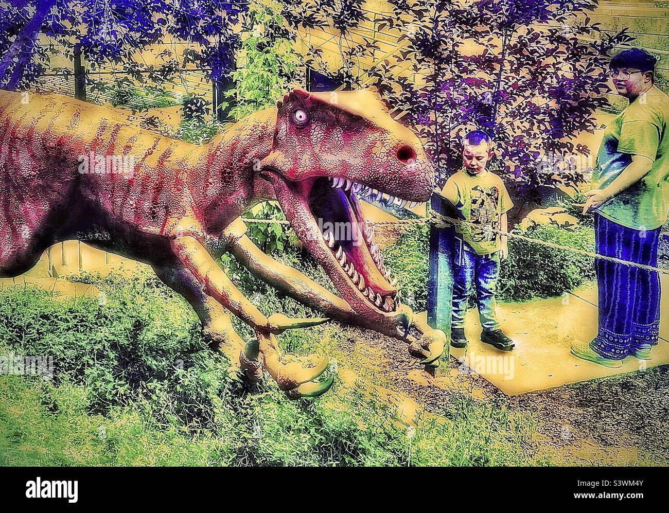 Pris dans les jardins de dinosaures, au musée d'histoire naturelle, ou au musée de dinosaures, à Vernal, Utah, États-Unis. Deux garçons se tiennent près de cette figure de Velociraptor. Effets de couleur et de grunge ajoutés numériquement. Banque D'Images