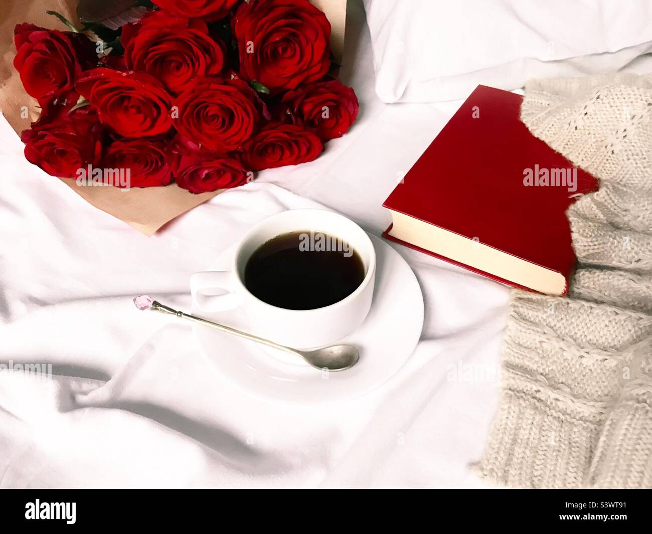 Tasse de café dans un lit confortable avec roses rouges, livre rouge et pull en maille - Image de stock capturée avec un smartphone
