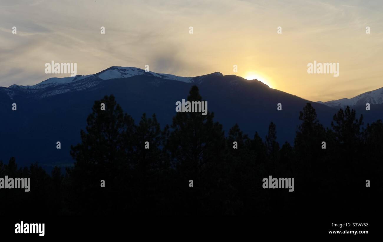 Contour spectaculaire des montagnes au crépuscule, avec le soleil derrière eux et sombre, silhoueté pins à peine visibles en premier plan. Montana, États-Unis - Image de stock capturée avec un smartphone