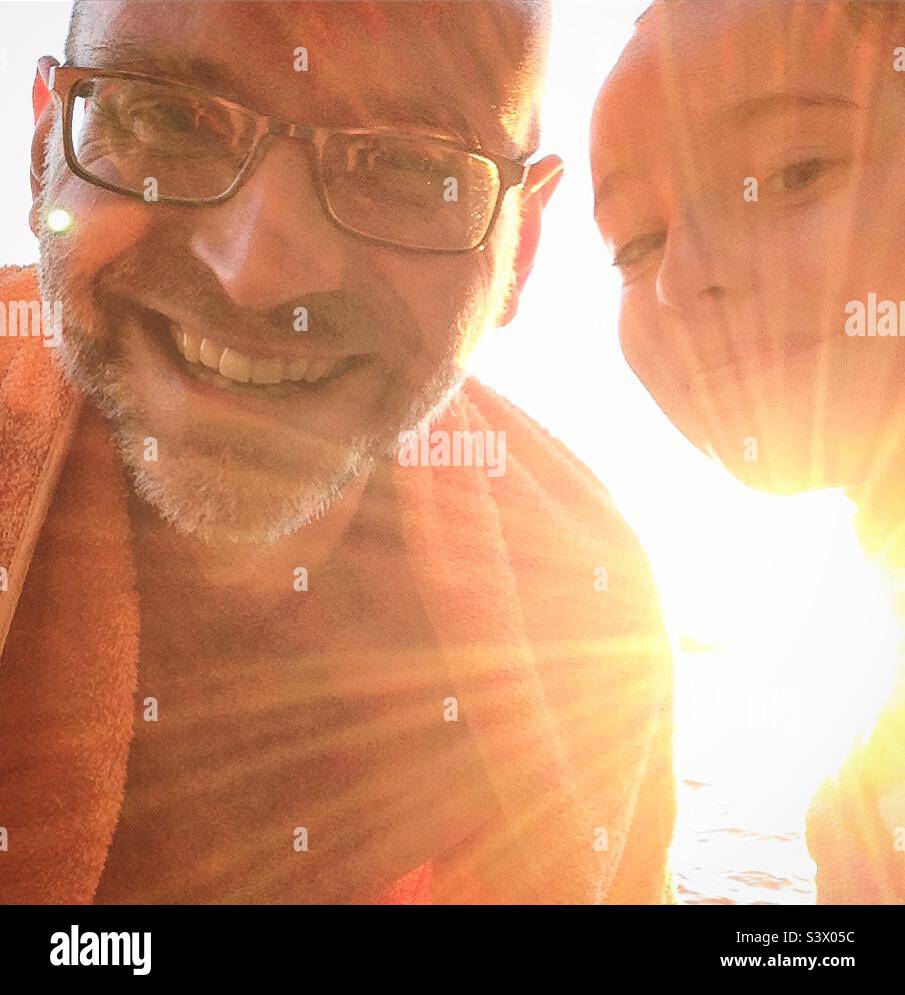 Père et fille partageant le temps de la famille heureux ensemble sur des vacances à la plage dans un selfie après une baignade dans le soleil d'été brillant Banque D'Images