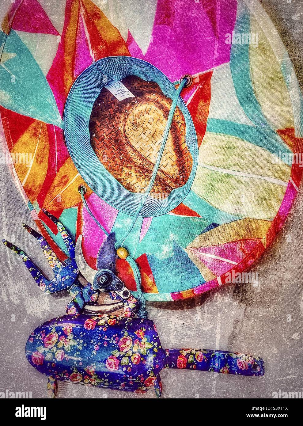 Les outils d’une jardinière féminine pour l’activité dans son jardin – un chapeau de paille coloré, des sécateurs de fleurs, une bêche et une griffe. Effet grunge ajouté numériquement à cette vie de plein air. - Image de stock capturée avec un smartphone