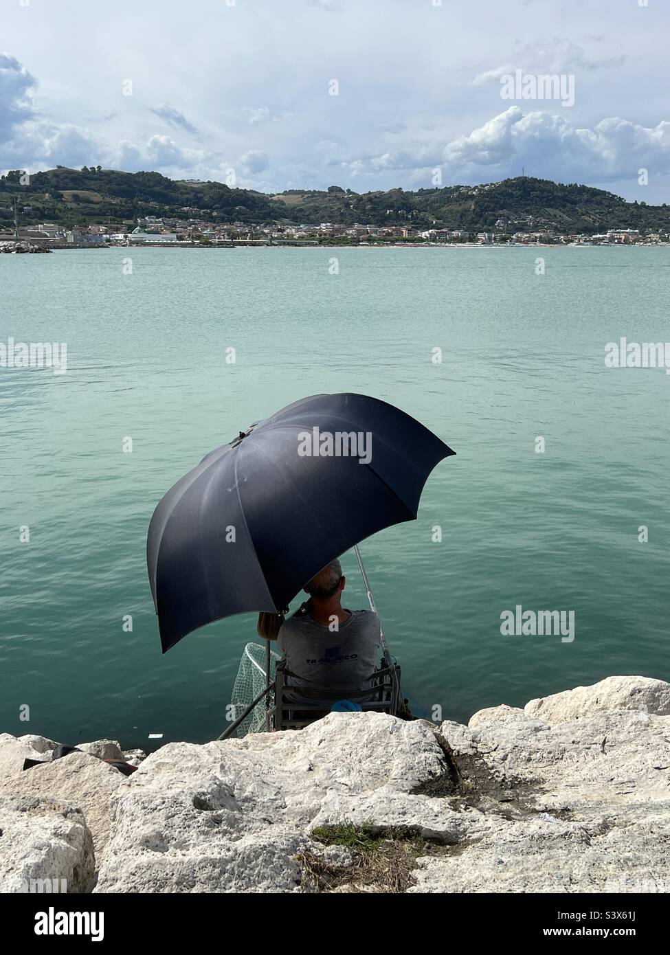 Pêcheur avec parasol devant la mer pendant un après-midi d'été Banque D'Images