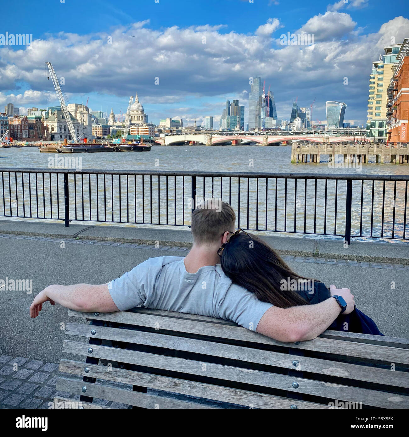 Un couple assis sur un banc sur la South Bank à Londres, regardant de façon romantique le long de la Tamise vers la City de Londres - Image de stock capturée avec un smartphone