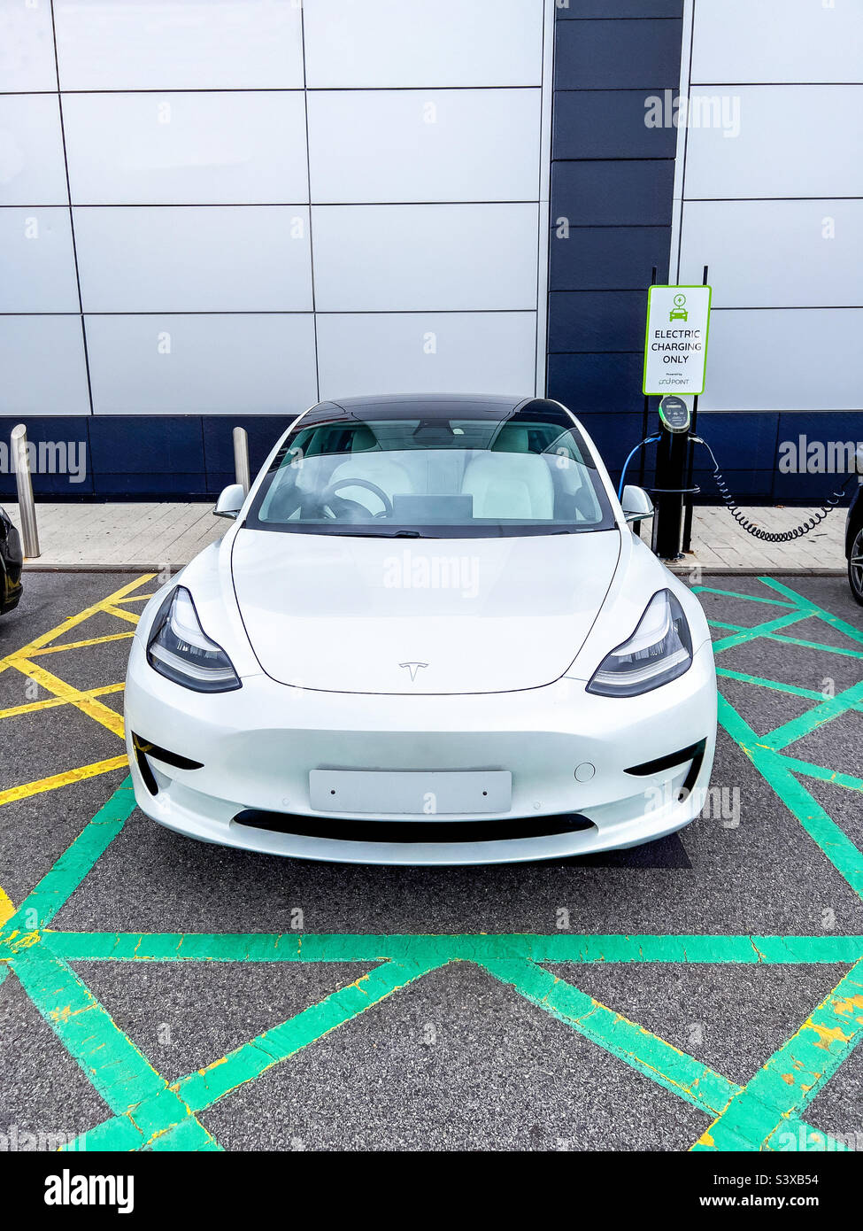 Tesla blanc modèle 3 branché à une station de charge électrique - Image de stock capturée avec un smartphone