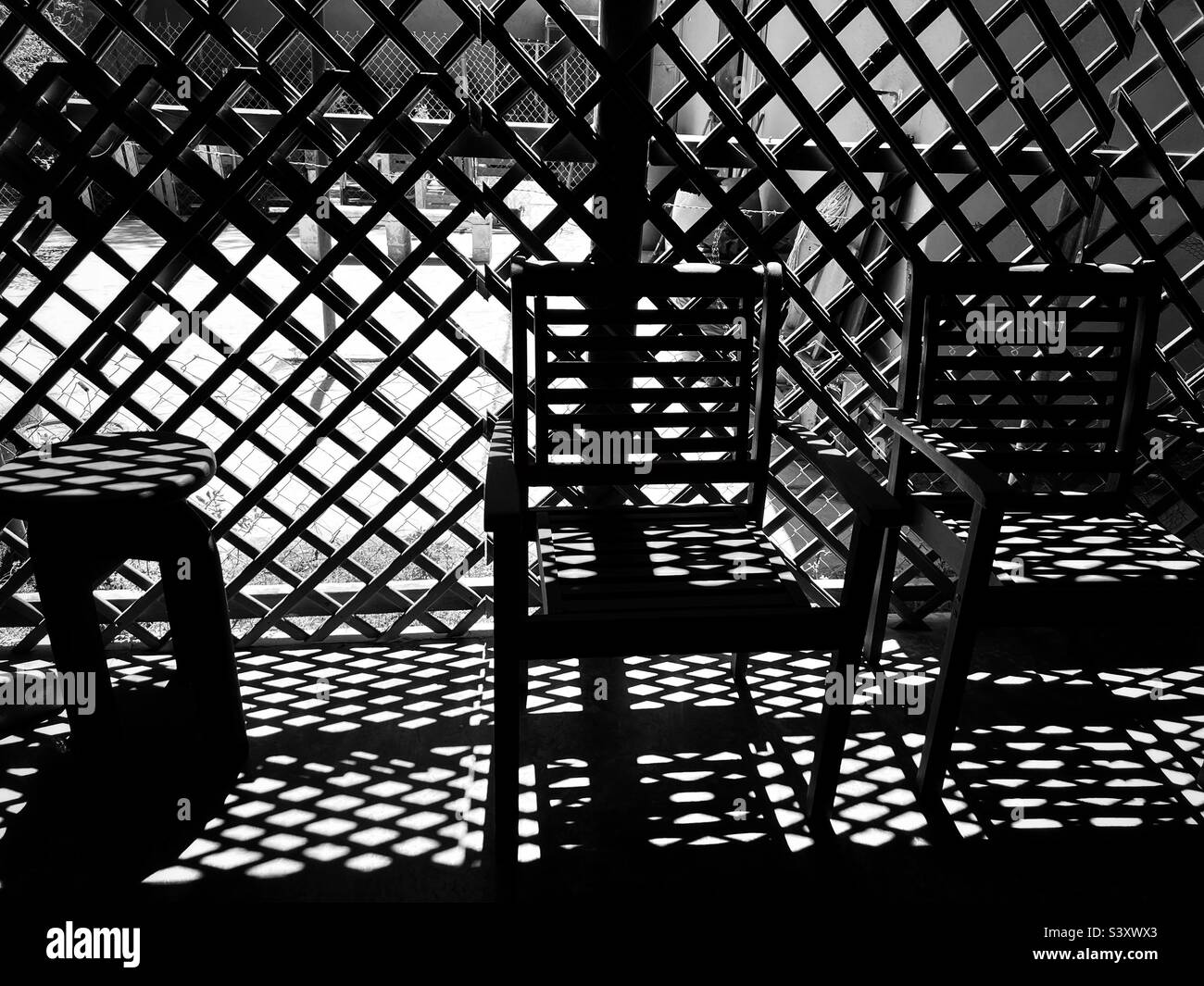 Beaucoup de lumière et d'ombres verser sur une paire de chaises devant un treillis pendant l'heure magique de lumière à Ensenada Mexique. Photographie abstraite en noir et blanc. Banque D'Images
