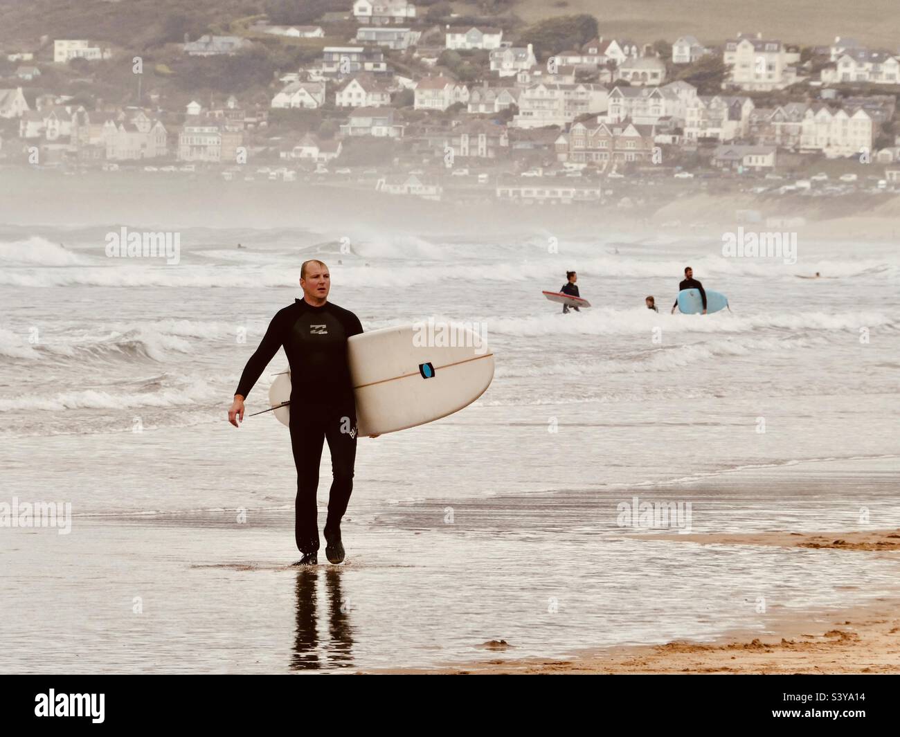 Un surfeur marche le long de la rive avec sa planche sous son bras à la plage de Putsborough dans le nord du Devon en Angleterre - Image de stock capturée avec un smartphone