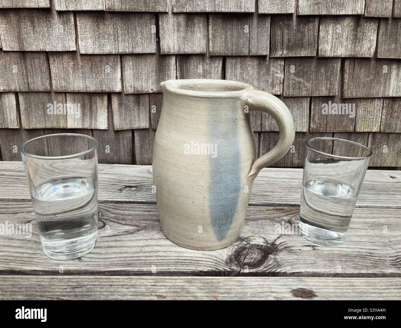 Deux verres d'eau et une cruche à eau en poterie sur une surface en bois devant un mur fait de bardeaux traditionnels Banque D'Images