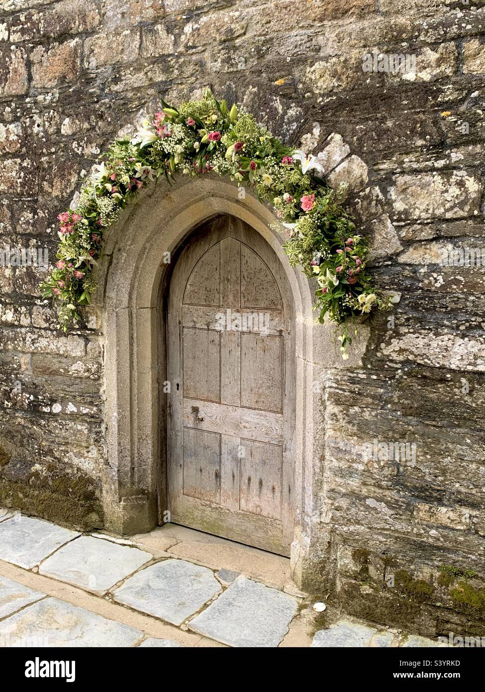 Magnifique jolie porte d'église en bois avec arche en pierre et belle décoration florale au-dessus de la porte pour un mariage, St juste à Roseland, Cornouailles, Angleterre Banque D'Images