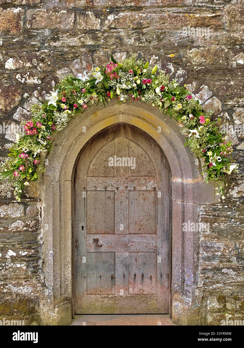 Magnifique arche normande en pierre sculptée avec une ancienne porte d'église en bois et une décoration florale pour un mariage à St juste dans l'église Roseland, en Cornouailles, en Angleterre, lors d'un après-midi d'été chaud Banque D'Images