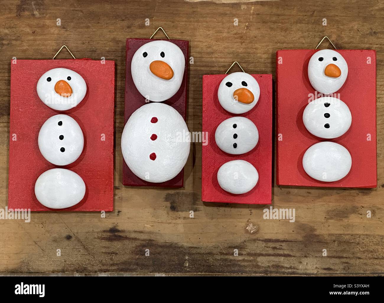 Des bonhommes de neige créatifs peints à la main avec des cailloux et des pierres sur des morceaux de bois Banque D'Images
