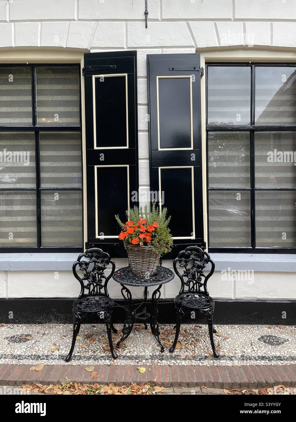 Table et chaises avec fleurs rouges à l'extérieur d'un bâtiment avec volets à Elburg, pays-Bas. Banque D'Images