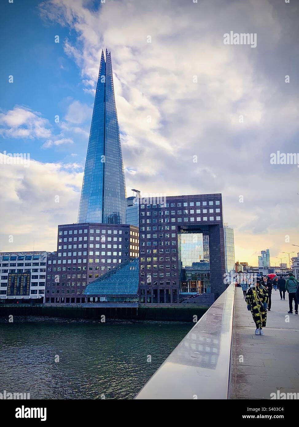 Lady en long manteau marchant le long du London Bridge avec le Shard derrière elle Banque D'Images
