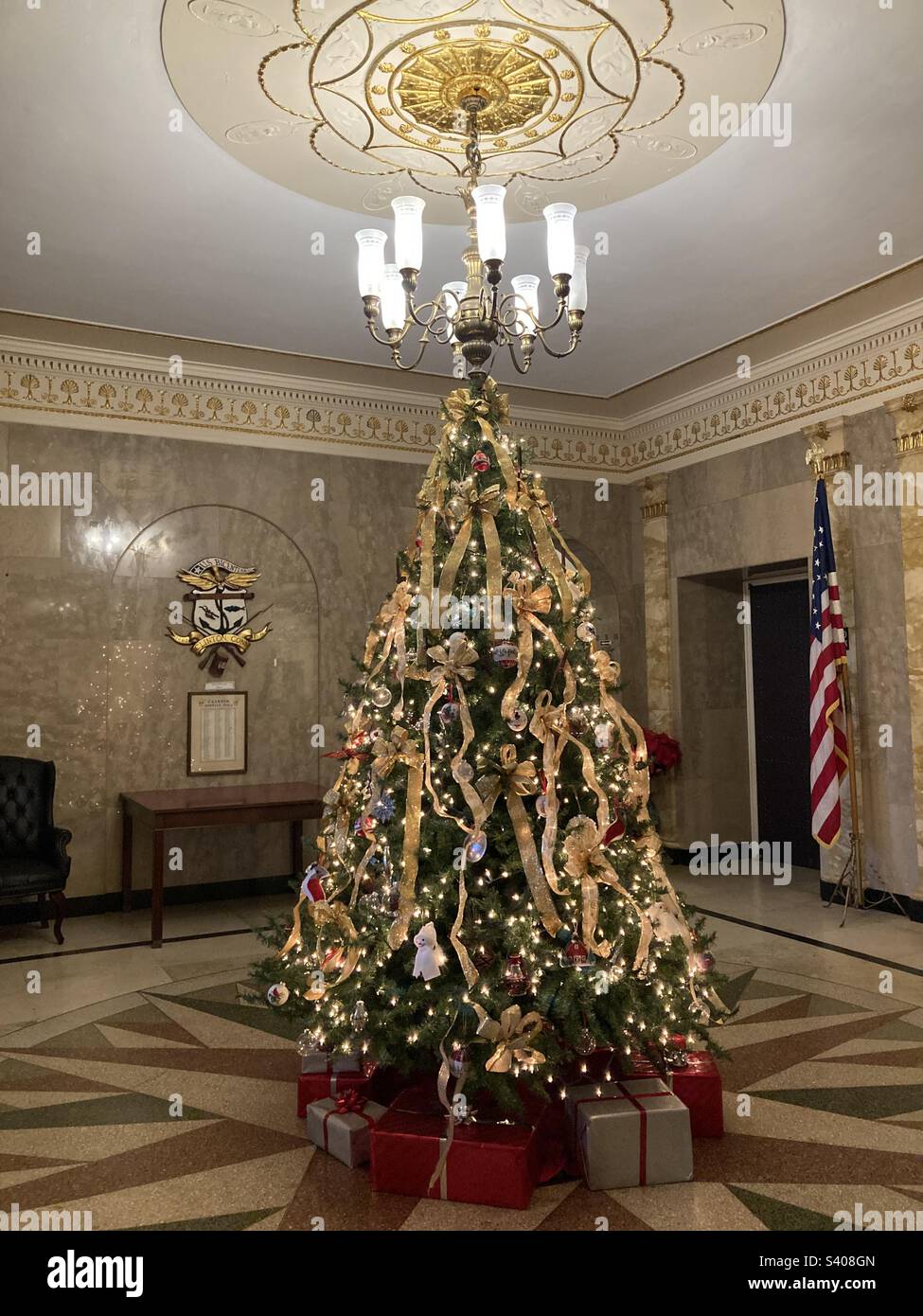 Arbre de Noël festif avec rubans à l'hôtel de ville de Clinton, Connecticut. Sous l'arbre sont rouge et argent présente. Et derrière se trouve un drapeau et une table des États-Unis. - Image de stock capturée avec un smartphone
