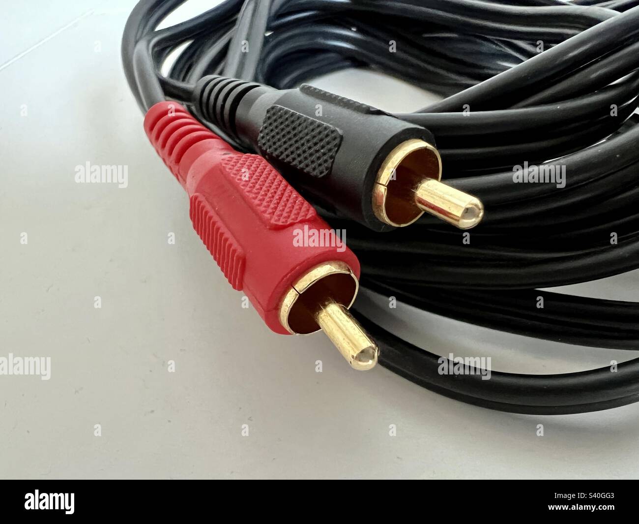 Macro View connecteurs phono plaqués or avec couvercles en plastique rouge et noir, à l'extrémité du câble audio noir, reposant sur une surface blanche et lisse Banque D'Images