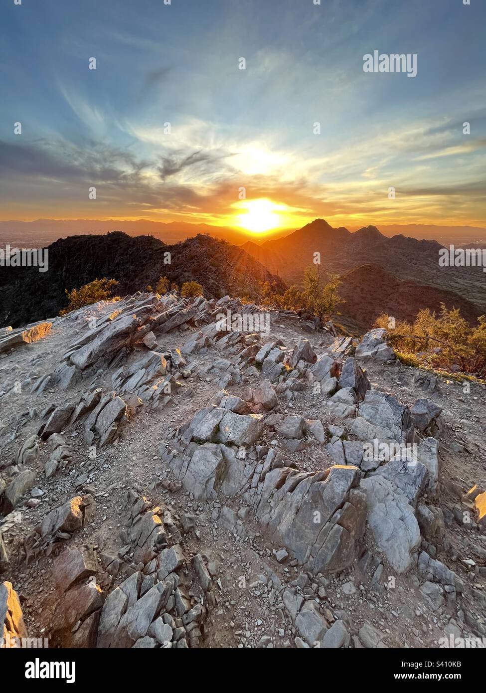 Le coucher de soleil doré à grand angle envoie de la lumière entre les pics de Phoenix Mountain Preserve, se faisant japper des rochers inclinés de Two bit Peak et plaçant la frange des buissons créosotes aglow, Scottsdale AZ Banque D'Images