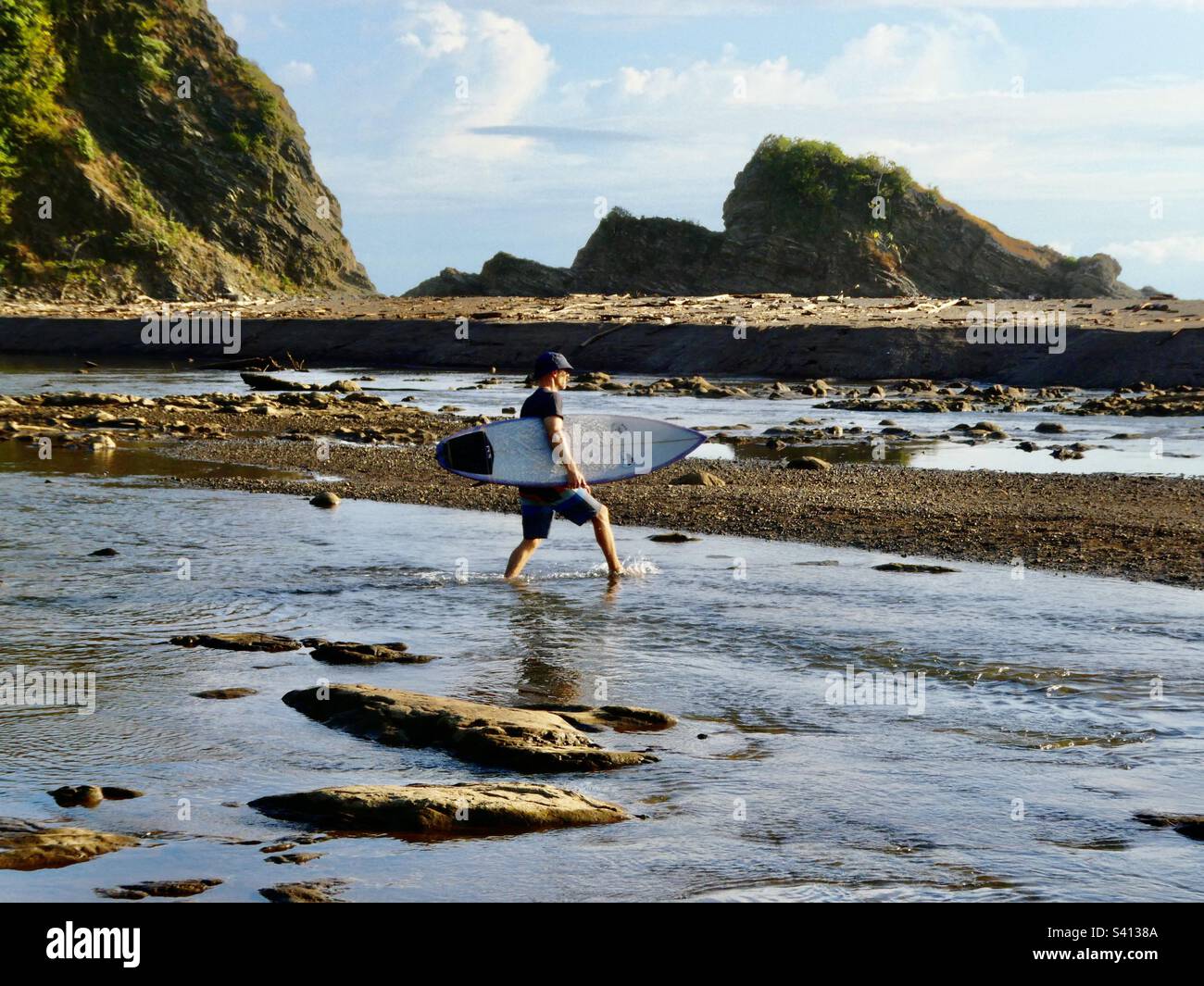 Un homme transporte une planche à voile sur une petite rivière jusqu'à la plage de Samara Costa Rica - Image de stock capturée avec un smartphone