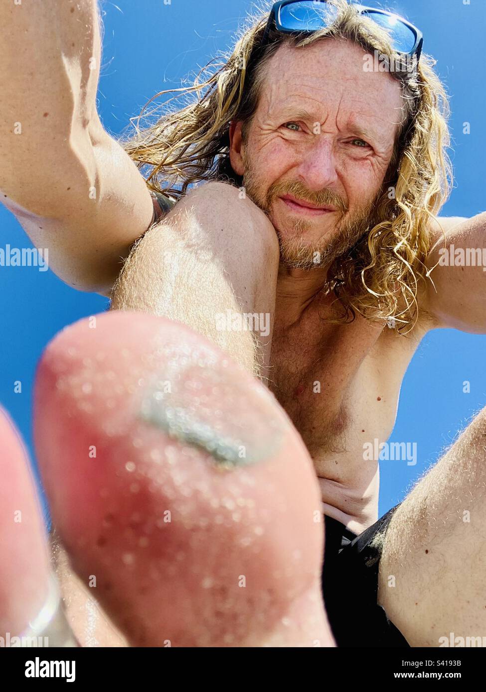 Un homme montre une photo d'un orteil blessé sur la plage par une journée ensoleillée Banque D'Images