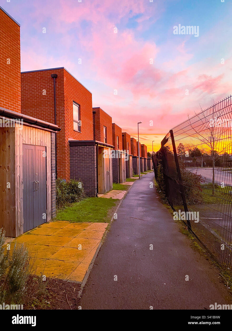 Marche sur un chemin avec des maisons de ville d'un côté et une clôture de l'autre au coucher du soleil. - Image de stock capturée avec un smartphone