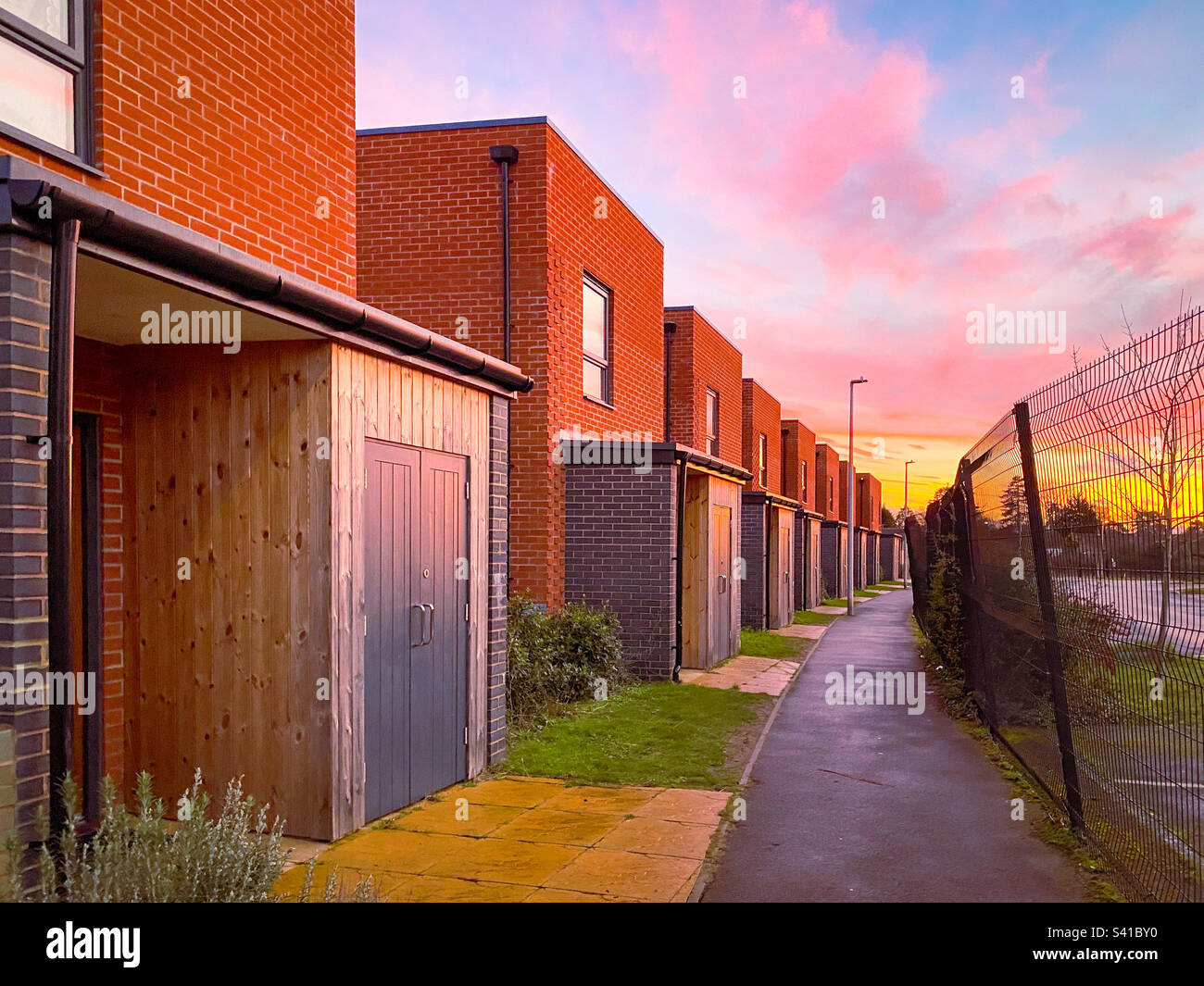 Marche sur un chemin avec des maisons de ville d'un côté et une clôture de l'autre au coucher du soleil. - Image de stock capturée avec un smartphone