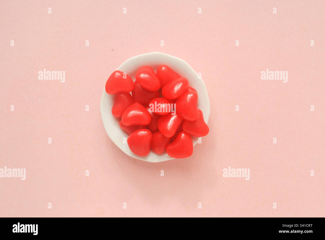 Une assiette blanche avec des bonbons à coeur rouge avec un fond rose Banque D'Images