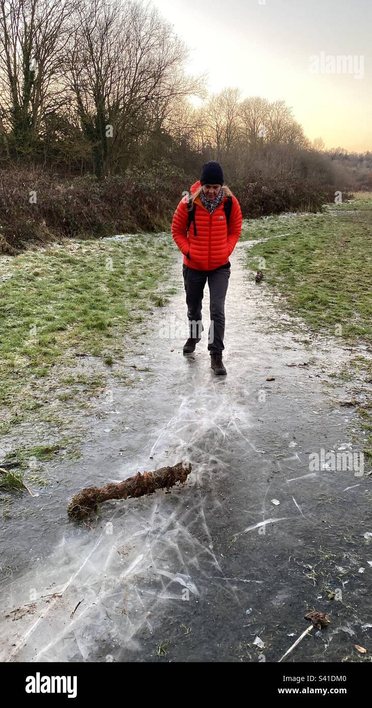 Une femme dans une veste orange marche soigneusement sur une glace au Royaume-Uni Banque D'Images