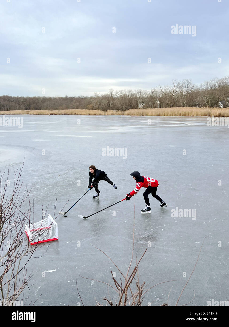 Deux garçons jouant au hockey sur glace sur un étang gelé dans le New Jersey, aux États-Unis. Banque D'Images