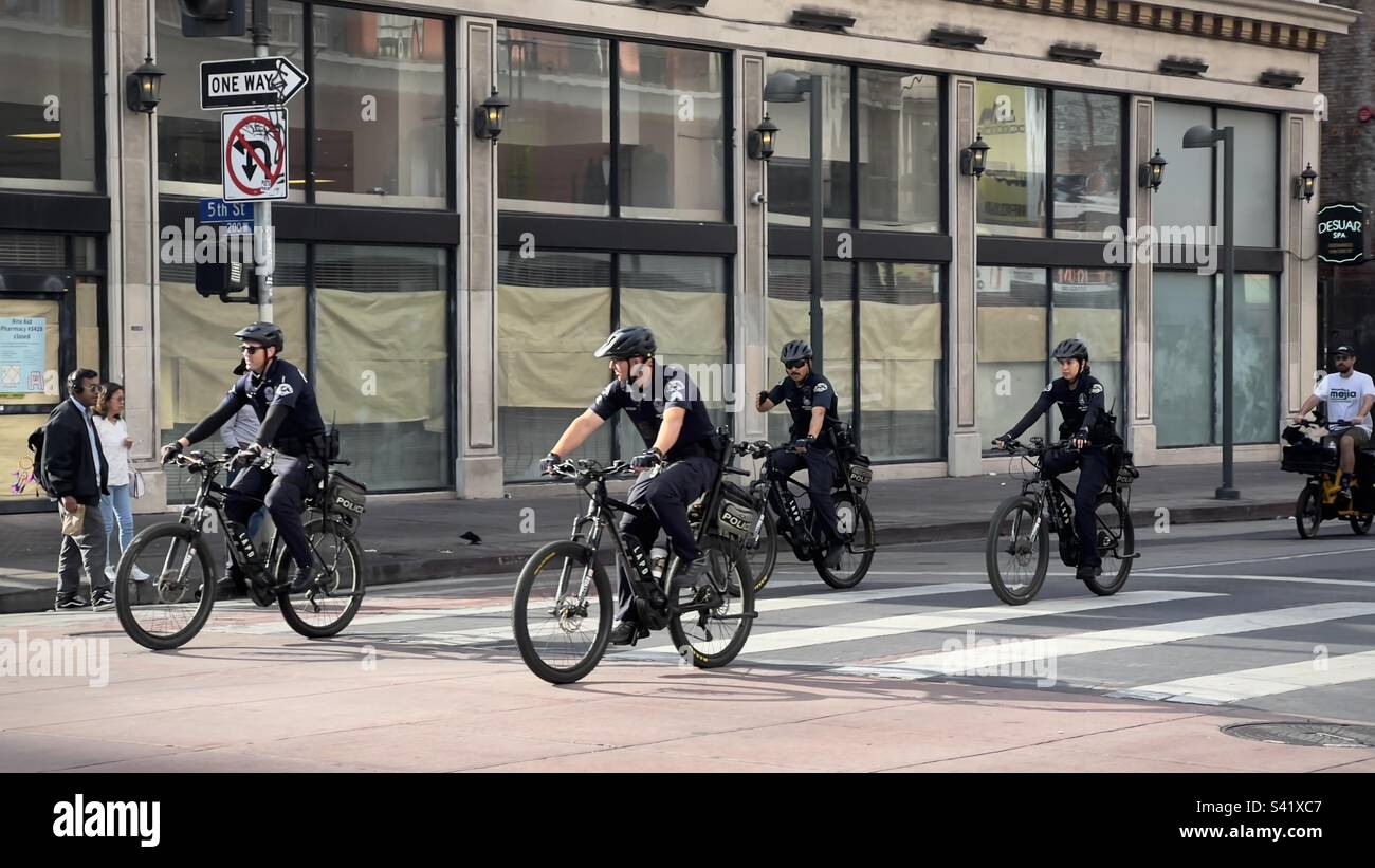 Groupe d'agents du service de police de Los Angeles sur des bicyclettes, passant devant un détaillant fermé dans le centre-ville de Los Angeles Banque D'Images