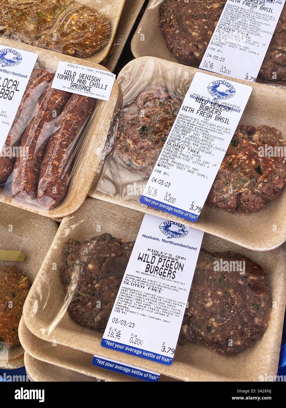 Spécialité produits de gibier sauvage et coupes de viande à vendre au marché agricole local, hamburger au pigeon de bois, hamburger à la venaison avec basilic et saucisse à la venaison avec tomate et piment - Image de stock capturée avec un smartphone
