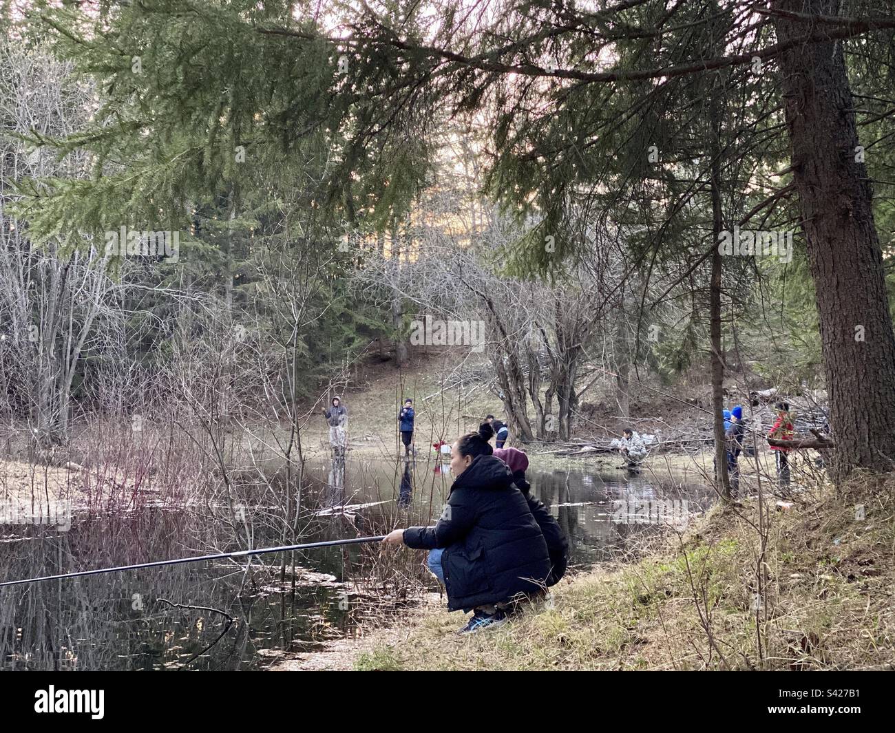 Beaucoup de jeunes pêcheurs avec des cannes à pêche de femmes, d'hommes et d'enfants Yakut pêchent sur la petite rivière de la taïga dans la forêt d'épinette Banque D'Images