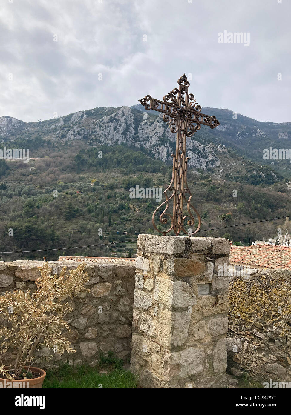 Croix de fer forgé complexe à Gorbio, en France, avec les Alpes françaises en arrière-plan. Banque D'Images