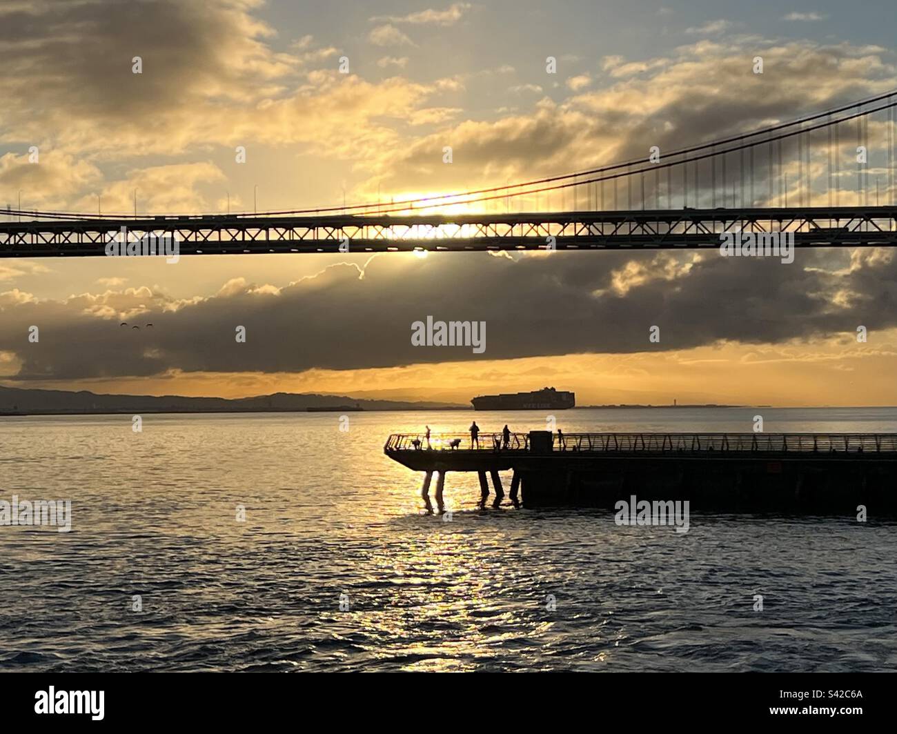 Les gens pêchent depuis une jetée publique avec le pont San Francisco - Oakland Bay Bridge et un grand navire au loin Banque D'Images