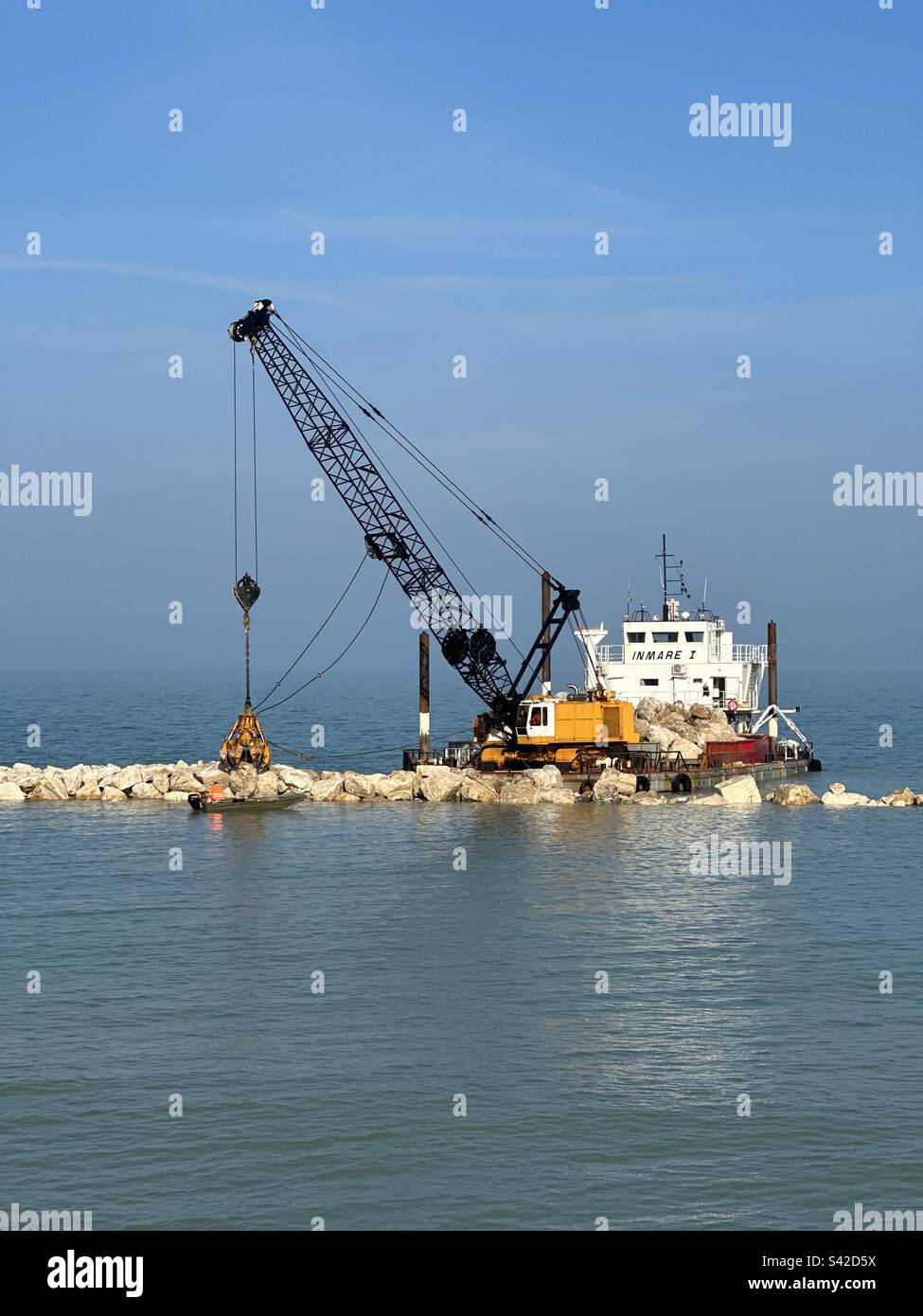 Barge avec grue soulevant des rochers pour un mur de mer le long du mur extérieur du port Banque D'Images