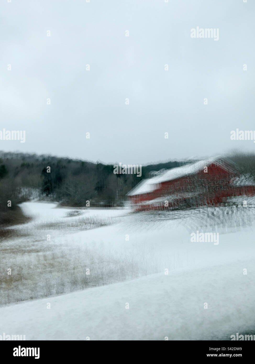 Bâtiments de ferme rouges dans un paysage enneigé du Vermont, aux États-Unis, photographiés à l'aide d'un obturateur lent provenant d'une voiture, entraînant un flou de mouvement. Banque D'Images