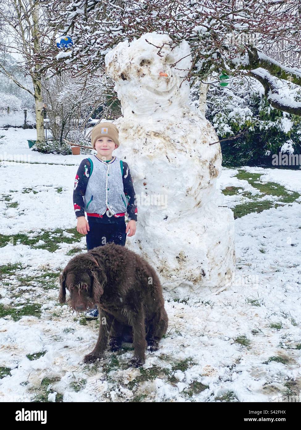 Garçon de six ans avec son chien de labradoodle dans la neige. Hampshire, Angleterre, Royaume-Uni. Banque D'Images