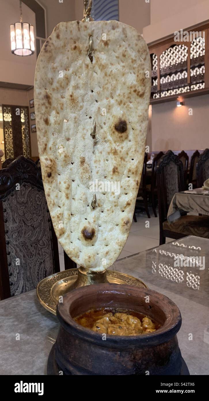 Pain naan afghan géant servi avec du curry de poulet dans un pot en argile Banque D'Images