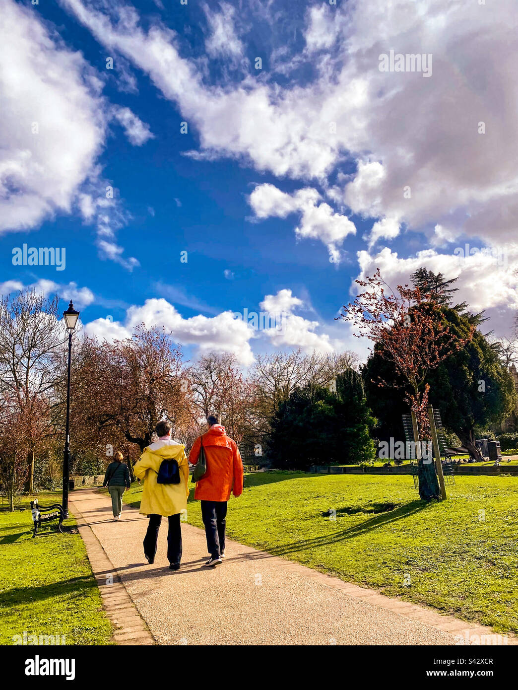 Un couple en imperméable rouge et jaune traverse un parc par une journée ensoleillée à Londres Banque D'Images