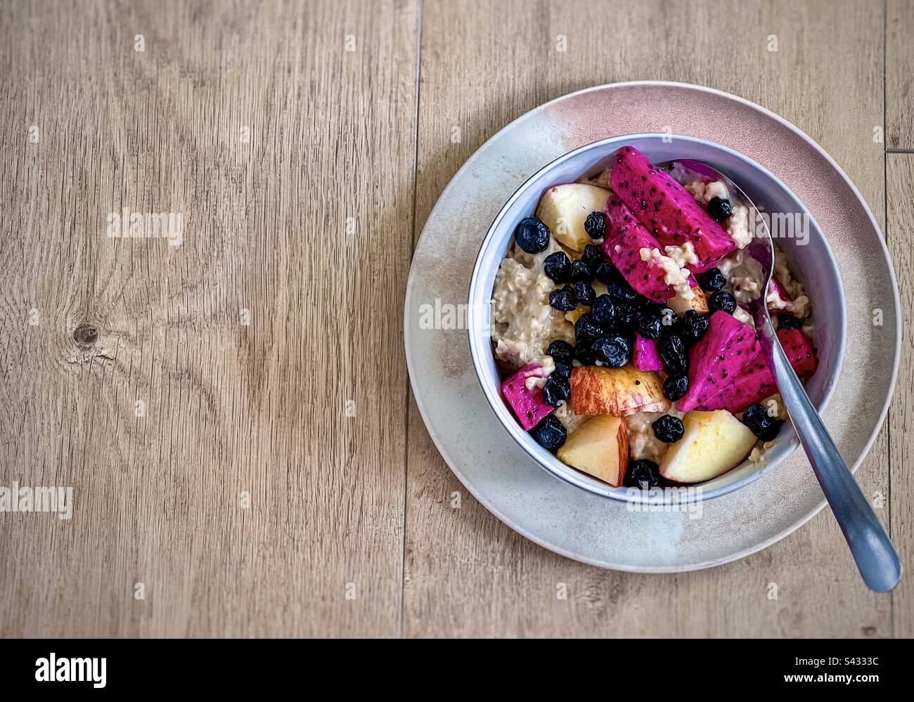 Directement au-dessus de la dose de flocons d'avoine avec des fruits frais et des bleuets séchés dans un bol avec une cuillère sur une assiette sur une table en bois. - Image de stock capturée avec un smartphone