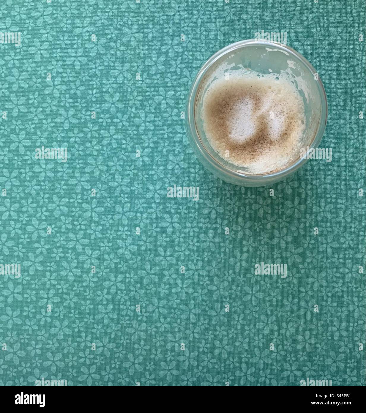 Image en gros plan d'un verre de cappuccino vide sur fond floral vert - Image de stock capturée avec un smartphone